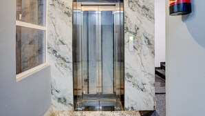 An elevator with a marble wall and a red fire extinguisher on the right.