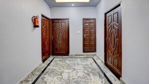 A hallway with three wooden doors, a fire extinguisher, and a ceiling with recessed lighting.