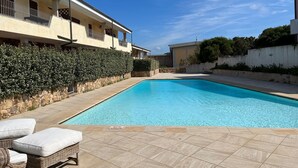 Una piscina con bordo piastrellato, circondata da un siepe e un muro in pietra.