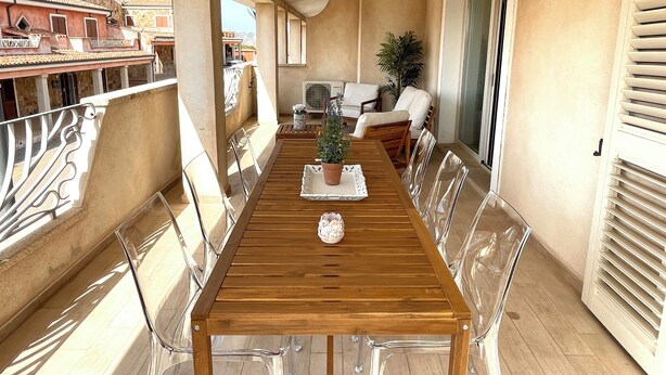 Un balcone con un tavolo di legno, sedie trasparenti e una pianta in vaso.