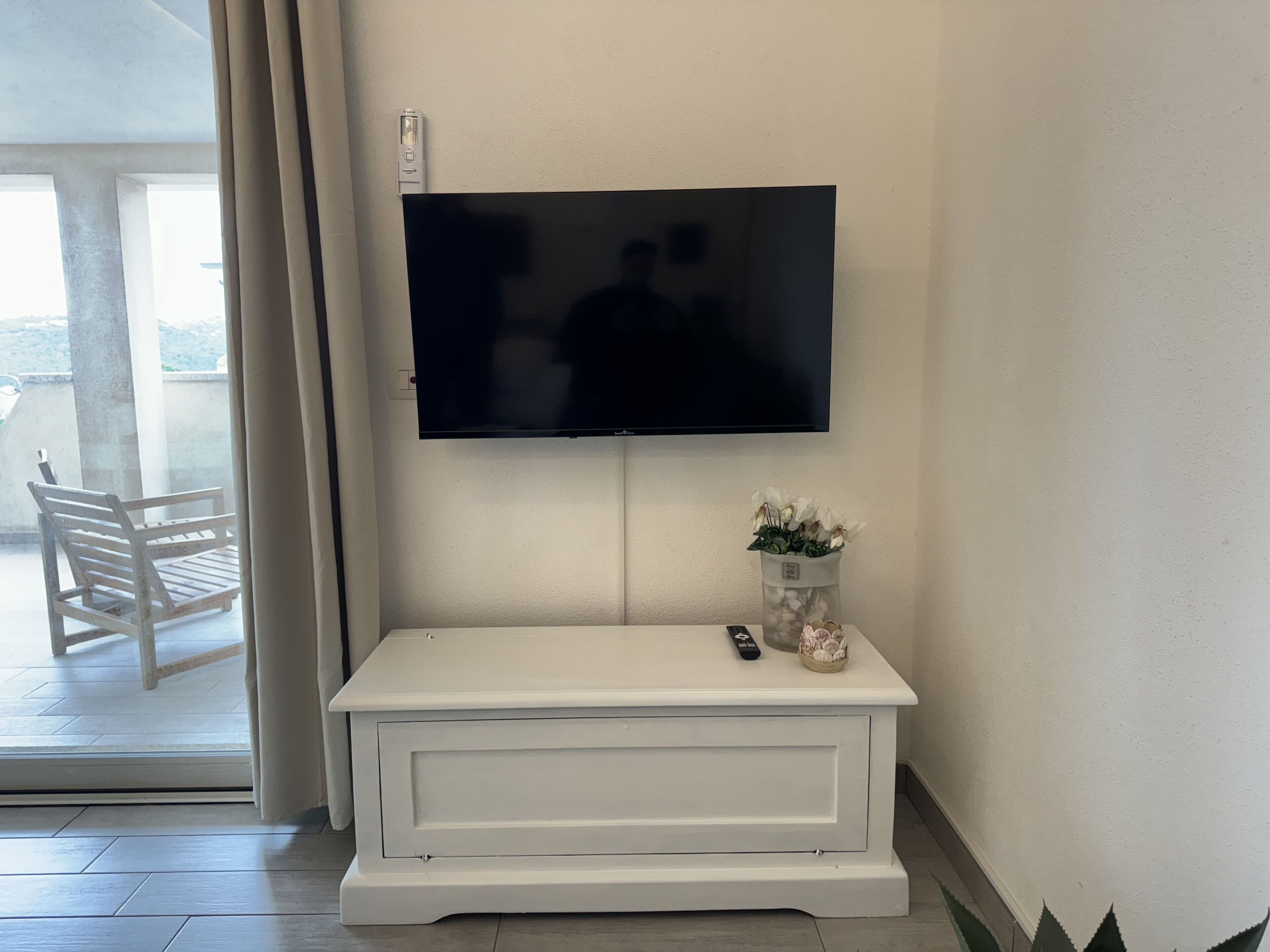 Una consola blanca con un televisor de pantalla plana montado encima, un control remoto y un pequeño objeto decorativo sobre la mesa.
