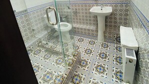 A bathroom with a glass shower enclosure, a toilet, a sink, and patterned tiles.