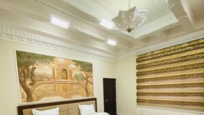 A hotel room with two beds, a large mural on the wall, a decorative ceiling, and a radiator.