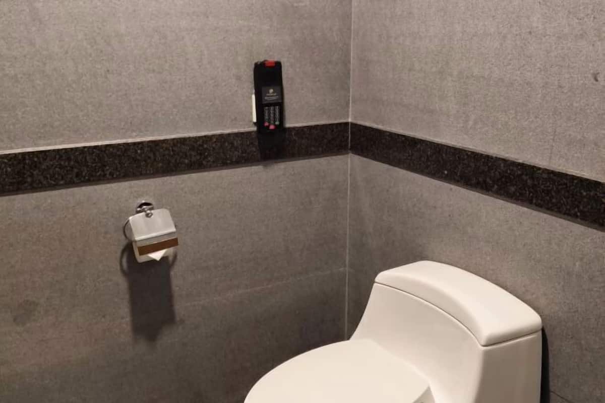 A restroom with a toilet, a hand dryer, and a soap dispenser on the wall.