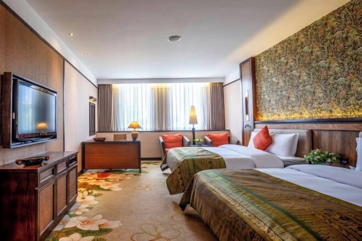 Une chambre d’hôtel équipée d’une télévision, de deux lits, d’un bureau et d’un grand mur décoré d’un motif floral.