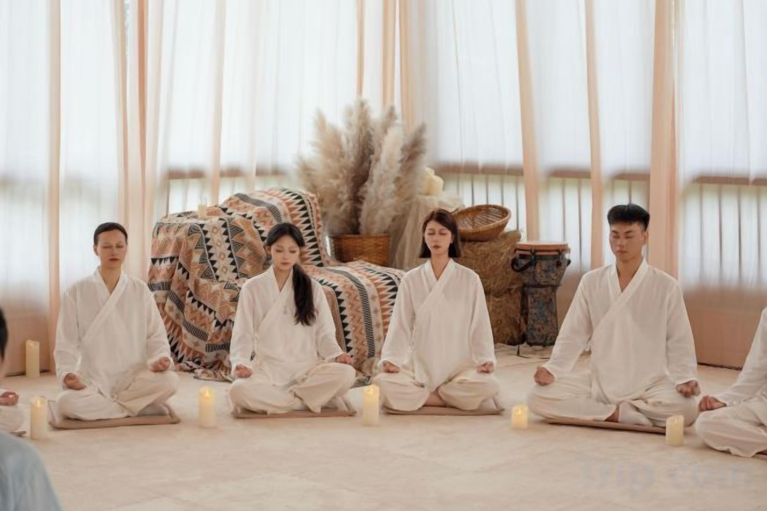 A group of individuals seated in a meditative pose in a room with a large window, a woven basket, and a patterned rug.