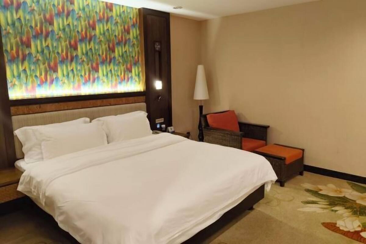 A hotel room with a large bed, a chair with an orange cushion, a lamp, and a colorful abstract painting on the wall.