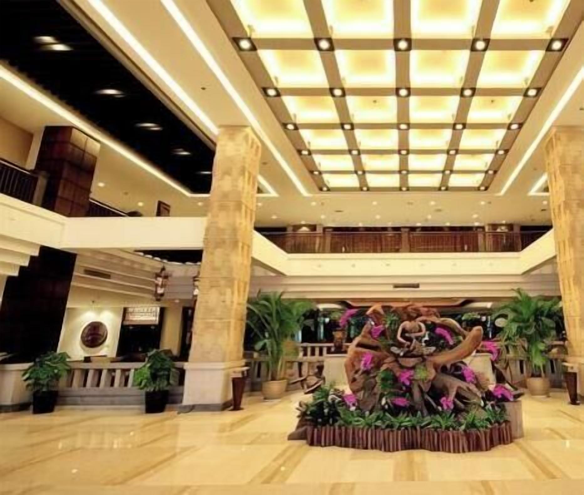 A spacious lobby with a central decorative sculpture, large pillars, and a high ceiling with recessed lighting.