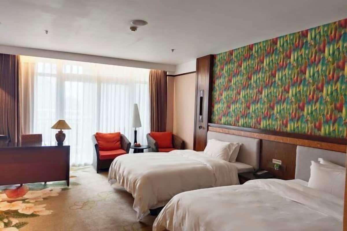 A hotel room with two beds, a desk, a chair, a lamp, and a colorful wall mural.