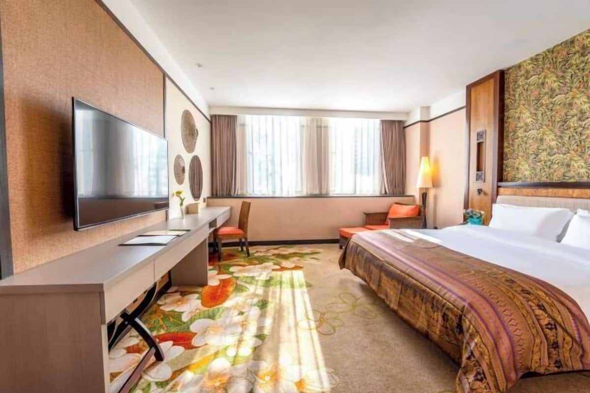 A hotel room with a bed, a desk, a TV, and a window with curtains.