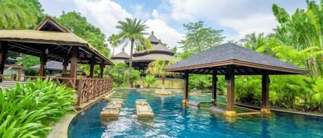 A swimming pool with lounge areas and thatched-roof structures surrounded by lush greenery.