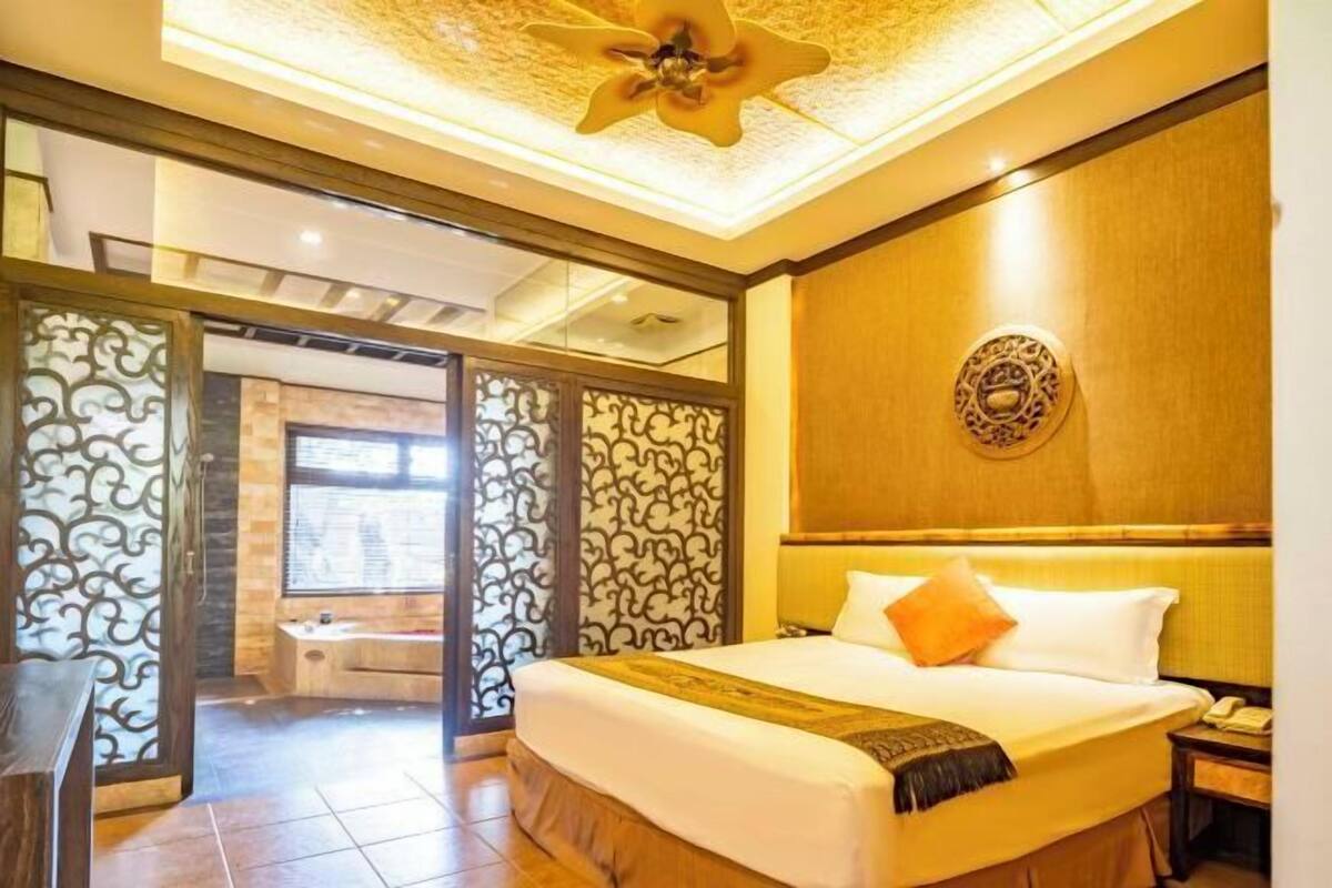 A hotel room with a bed, a wooden headboard, a ceiling fan, and a decorative wall panel.