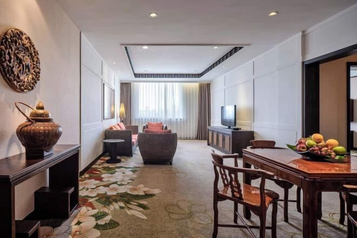 A hotel room with a dining area, a sofa, a TV, and a decorative vase.