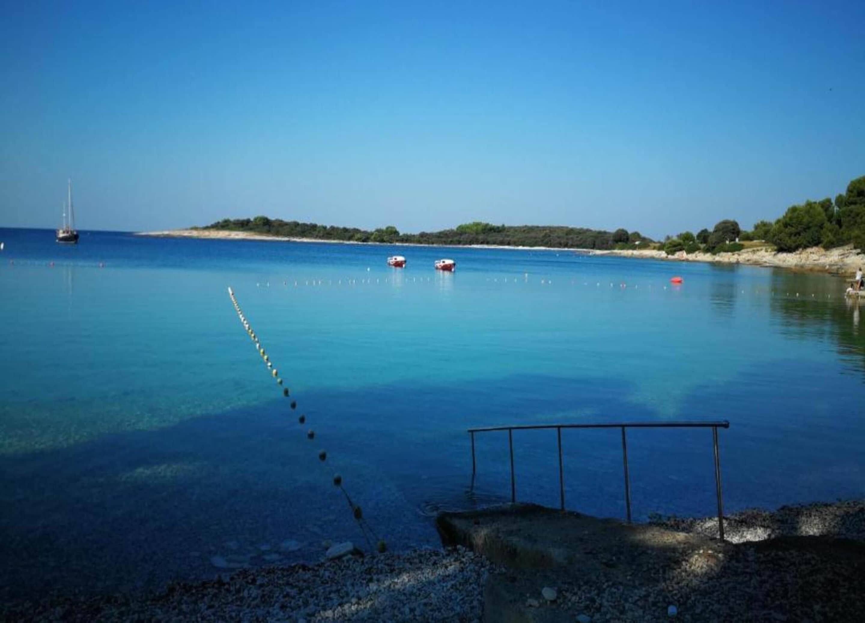 Une zone côtière paisible, avec une eau bleue et limpide, une canne à pêche et des bateaux visibles au loin.