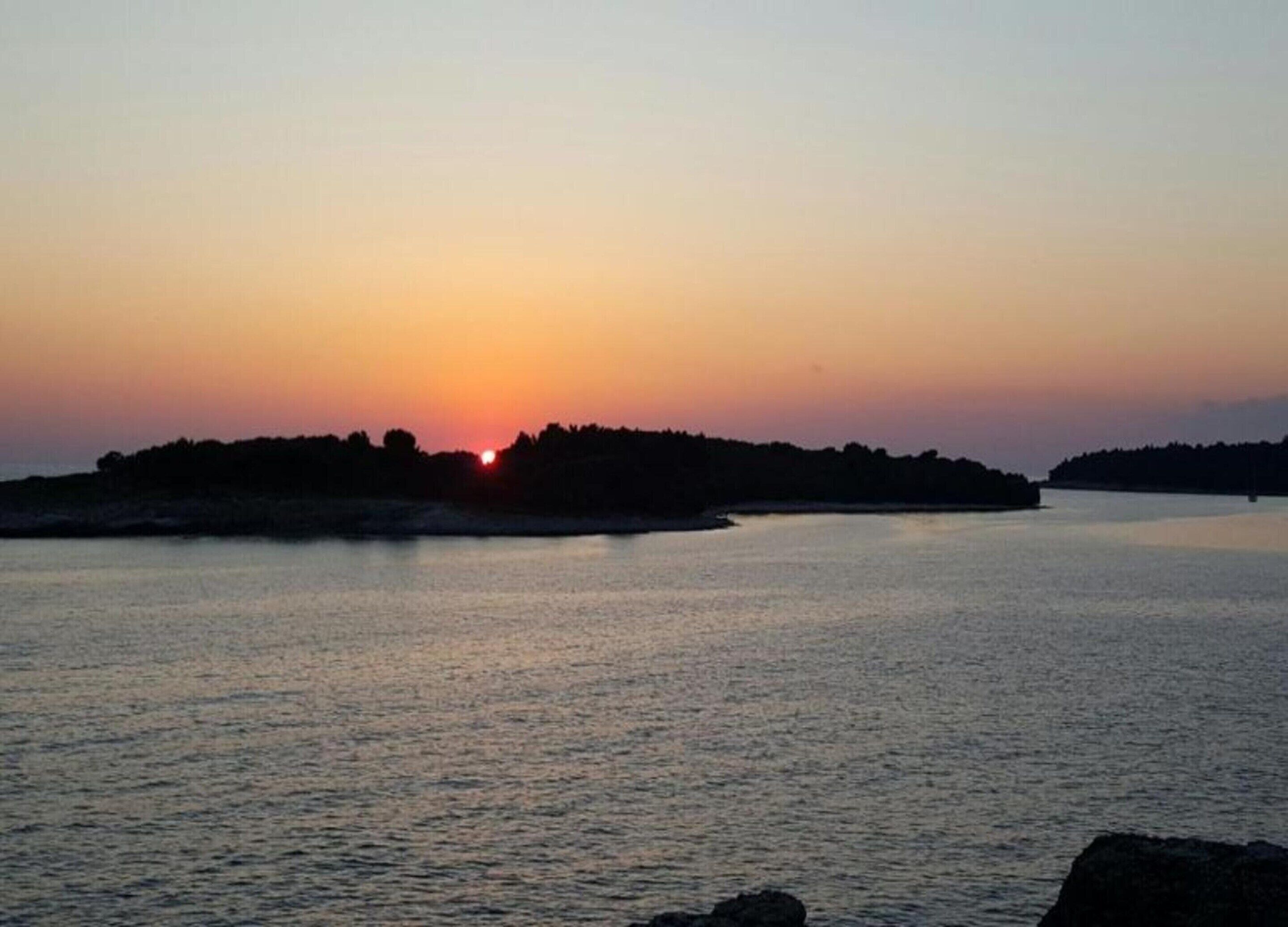A sunset over a calm body of water with a distant landmass.