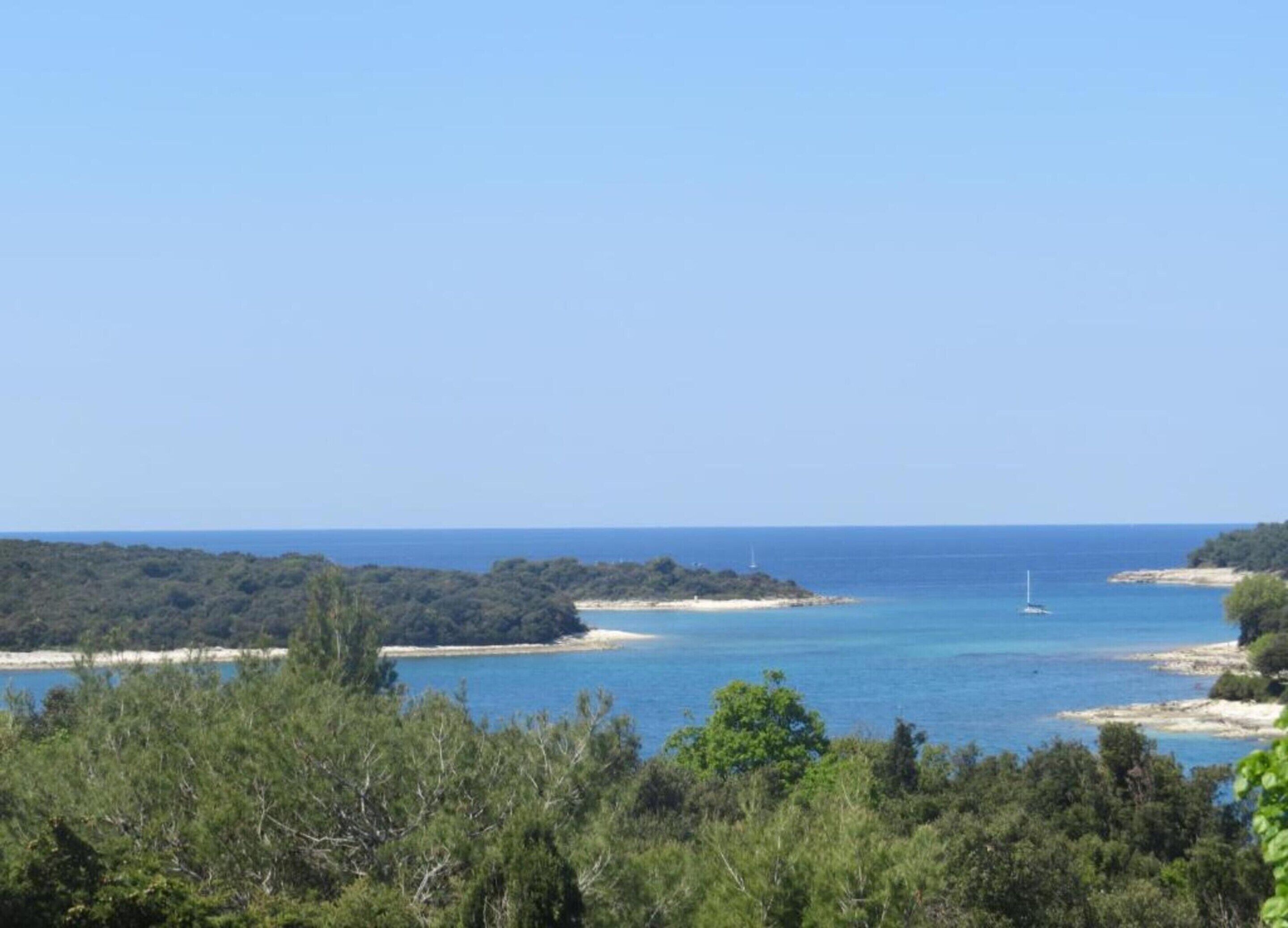A coastal landscape with a clear view of the sea, a sandy beach, and dense greenery.