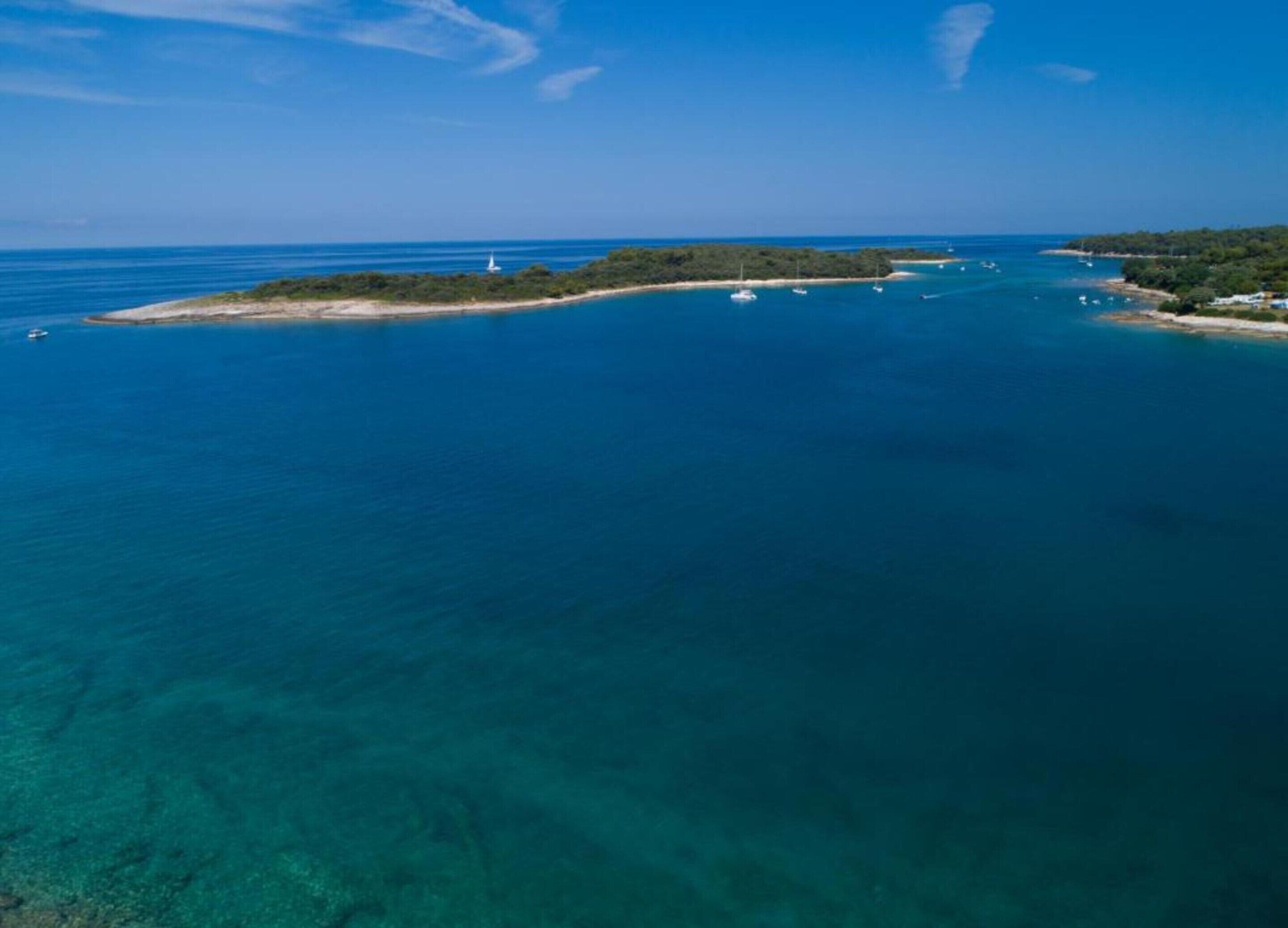 An aerial view of a coastal area with clear blue waters, a lighthouse, and a small island with dense vegetation.