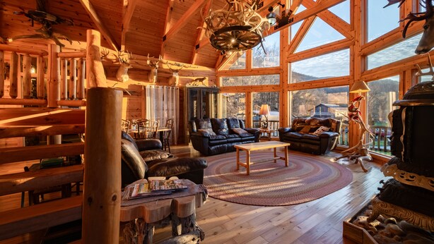 A log cabin interior with a large wooden ceiling, a fireplace, leather furniture, and a view of the outdoors. - Rocky Mt Lodge - Hot tub, Firepit, Fishing, Floating, Large Mountian Getaway (Elkins)
