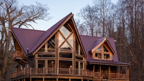 A log cabin with a large deck and multiple windows, surrounded by trees. - Rocky Mt Lodge - Hot tub, Firepit, Fishing, Floating, Large Mountian Getaway (Elkins)