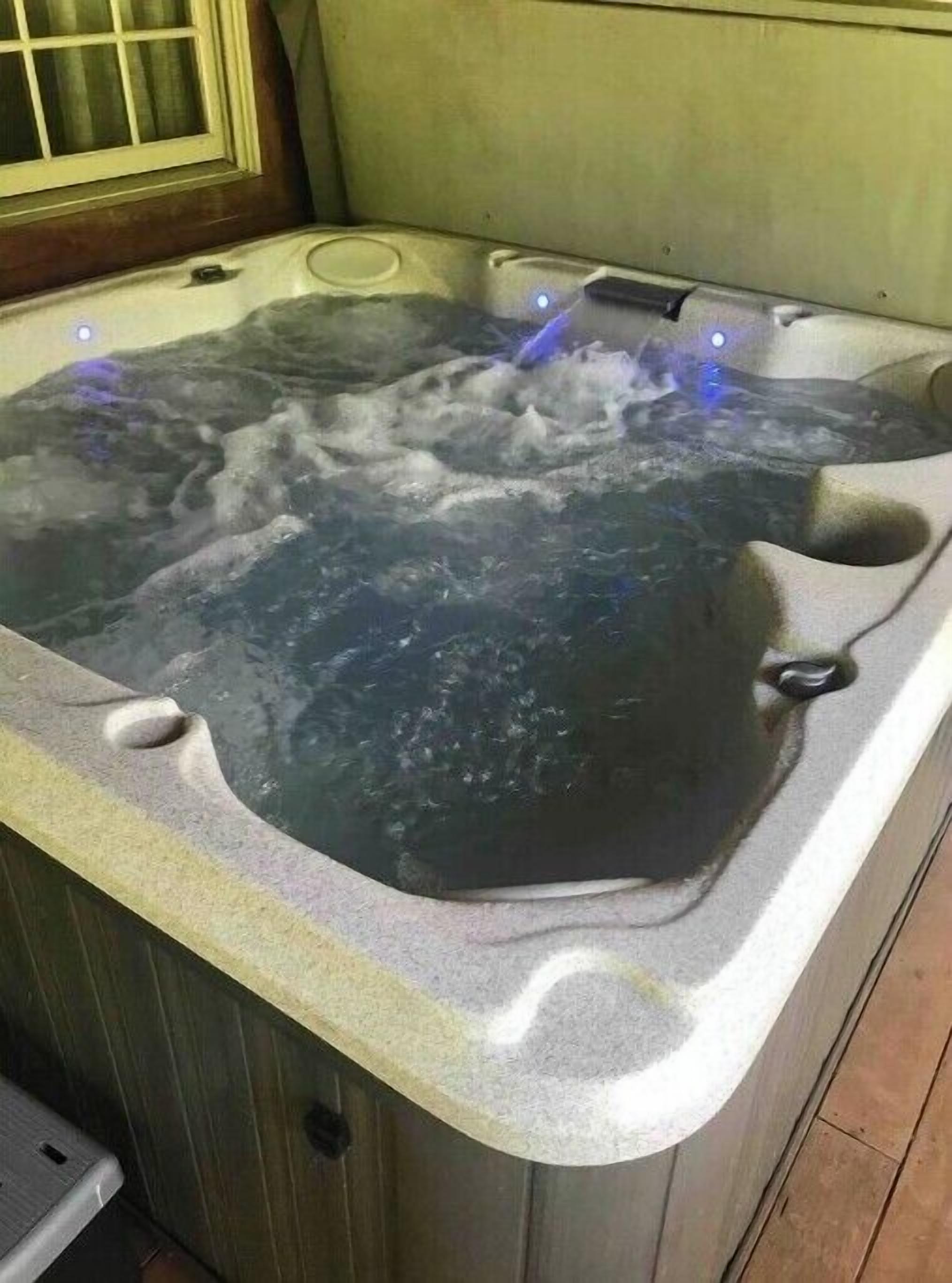 A hot tub with water jets, a wooden exterior, and a window with curtains.