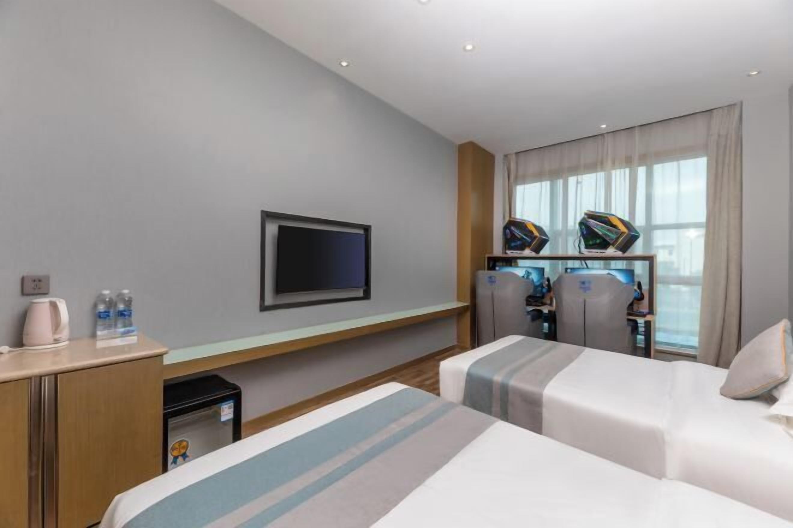 Habitación de hotel con dos camas, televisión, escritorio con computadora y ventana con cortinas.