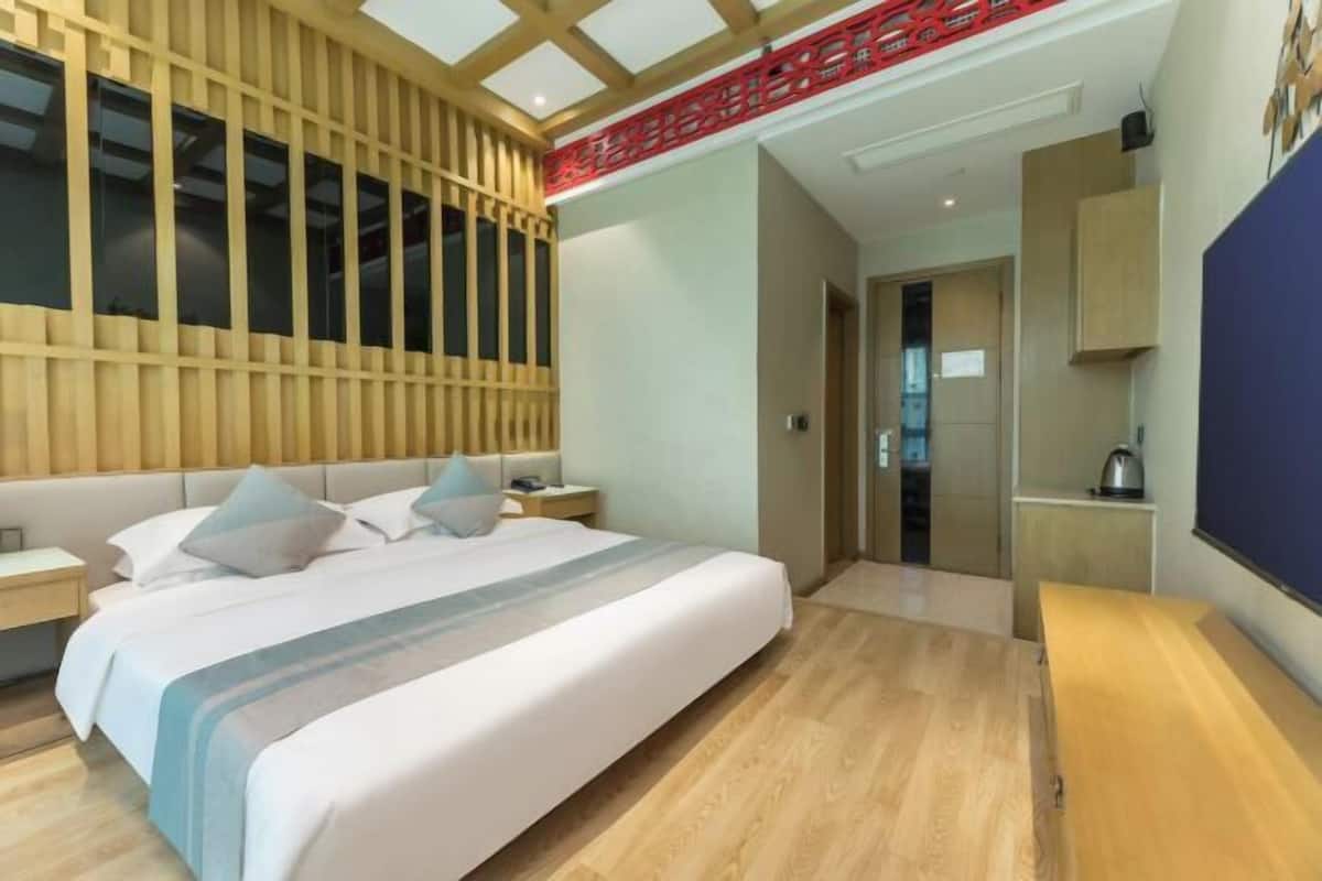 Habitación de hotel moderna con una cama grande, paneles de madera en la pared, techo decorativo rojo y vistas a la ciudad.