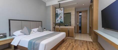 A modern hotel room with a large bed, wooden flooring, a TV, and a bathroom with a mirror and sink.