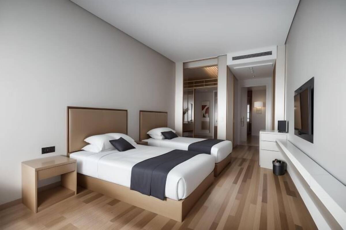 Una habitación de hotel moderna con dos camas, una mesita de noche, un televisor y un vestidor.