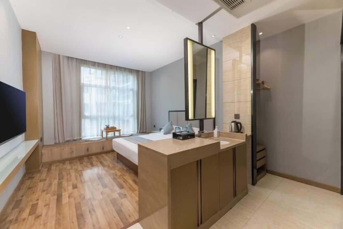 Habitación de hotel moderna con una cama grande, un escritorio empotrado con espejo, ducha y un ventanal con cortinas.