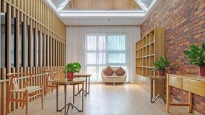 A modern interior with a wooden floor, a high ceiling with skylight, a brick wall, and a seating area with a cushioned chair and a small table with a plant. - Crossing E-sports Hotel (Wenzhou)