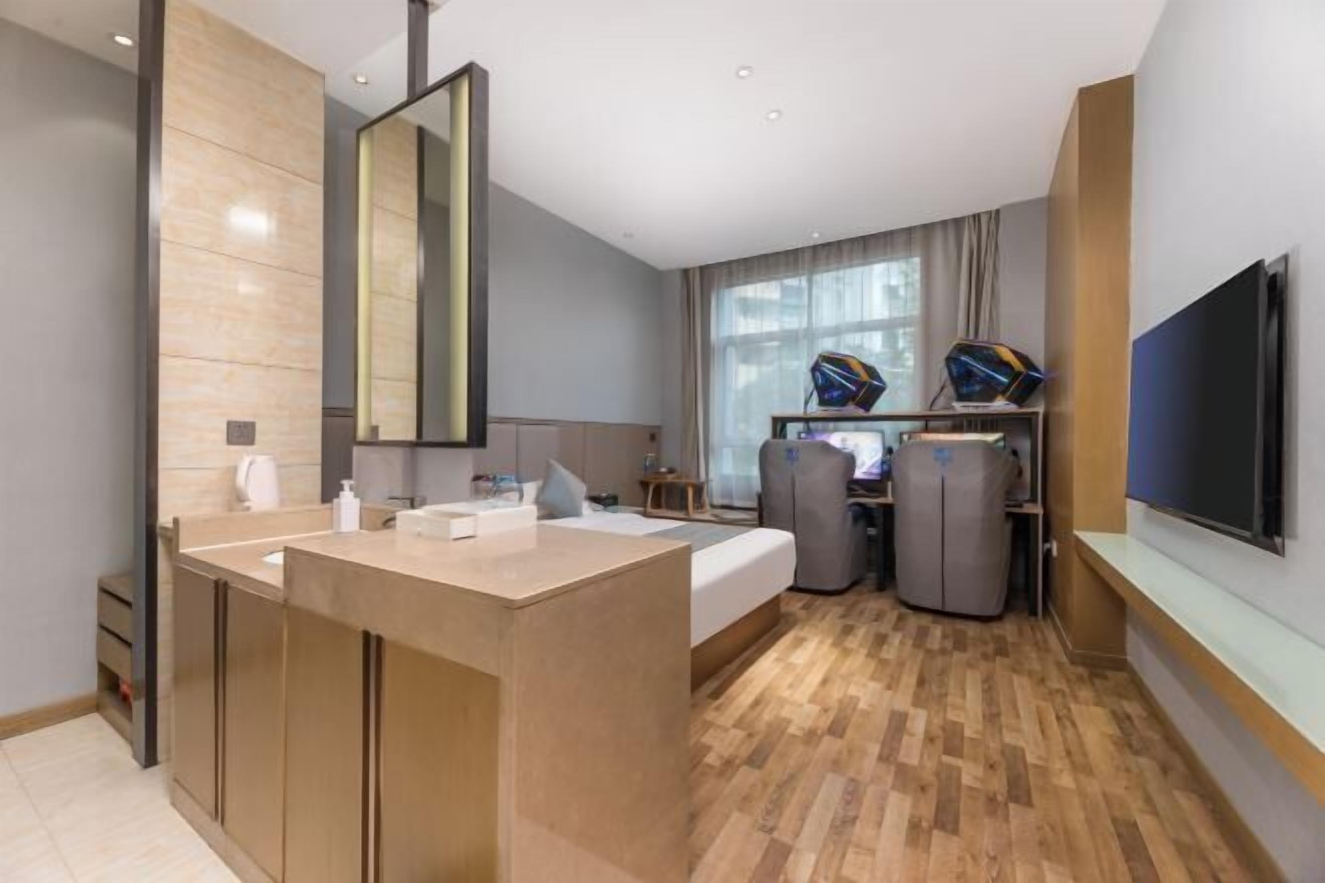 A modern hotel room with a large mirror, a bed, a desk with two chairs, a TV, and a minibar.