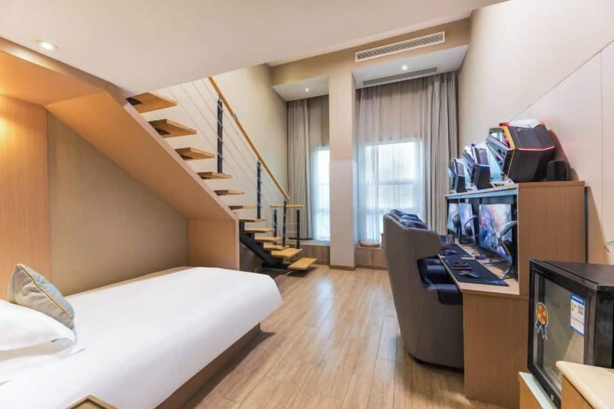 Una habitación de hotel con una cama, un escritorio con varios monitores, una silla y una escalera.
