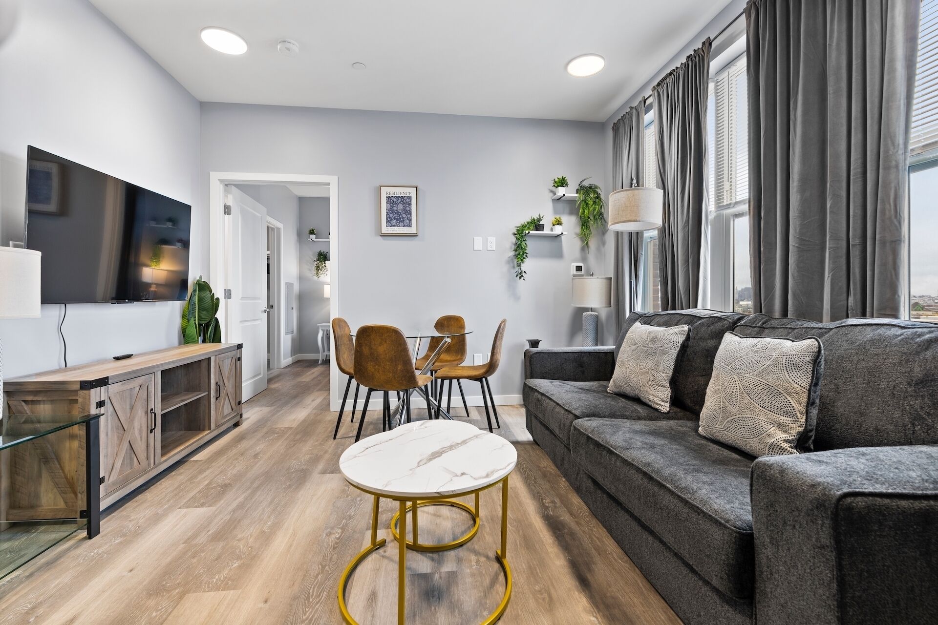 Ein modernes Wohnzimmer mit einem grauen Sofa, einem Marmor-Couchtisch und einem an der Wand befestigten Fernseher.