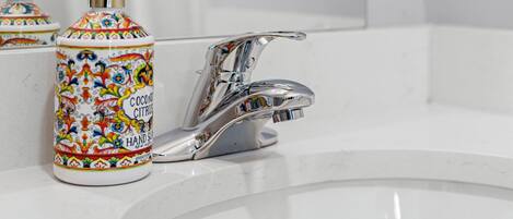 A bathroom sink with a chrome faucet and a colorful hand soap dispenser.