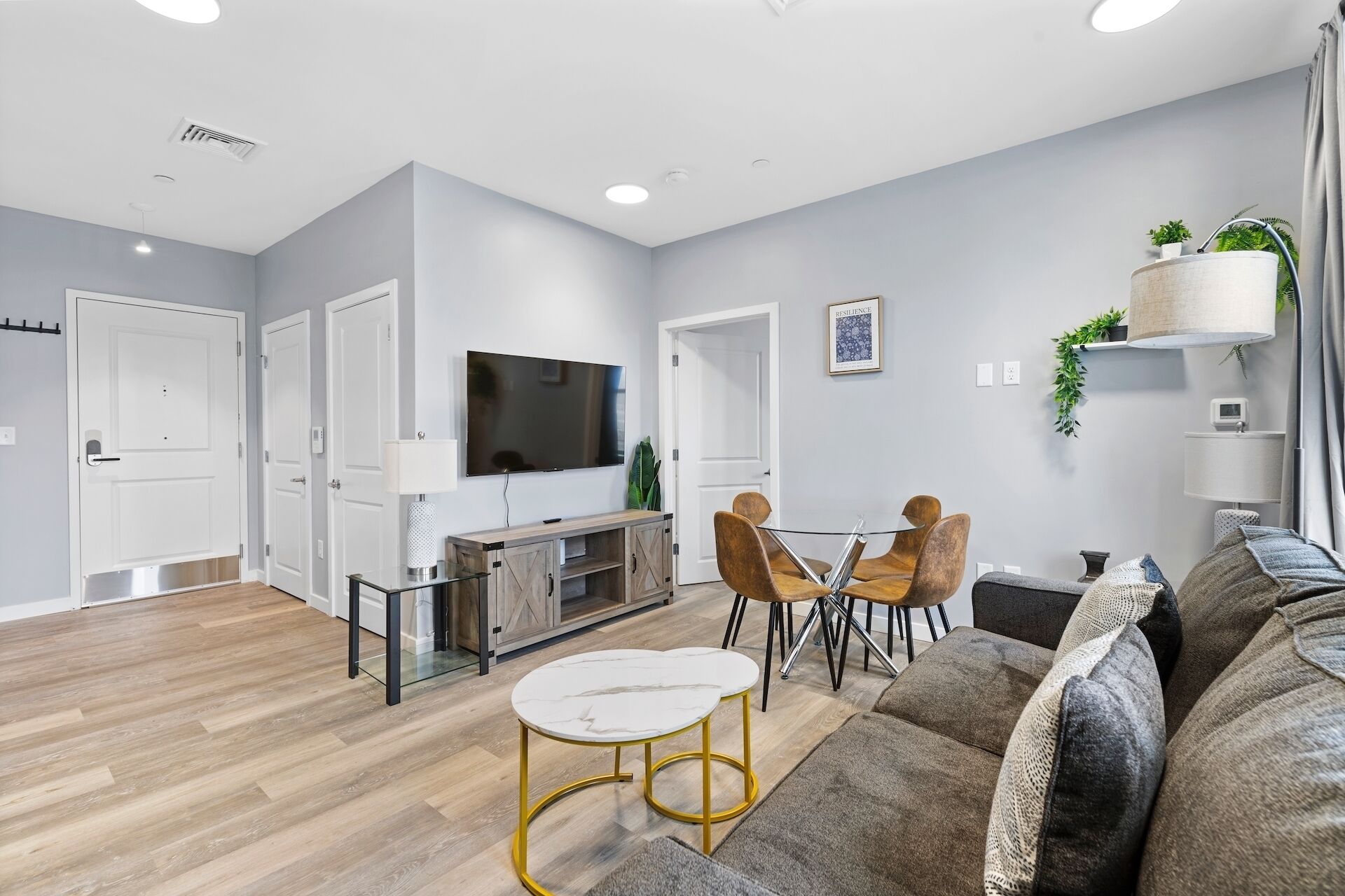 A modern living room with a flat-screen TV, wooden flooring, a glass coffee table, and a sofa.