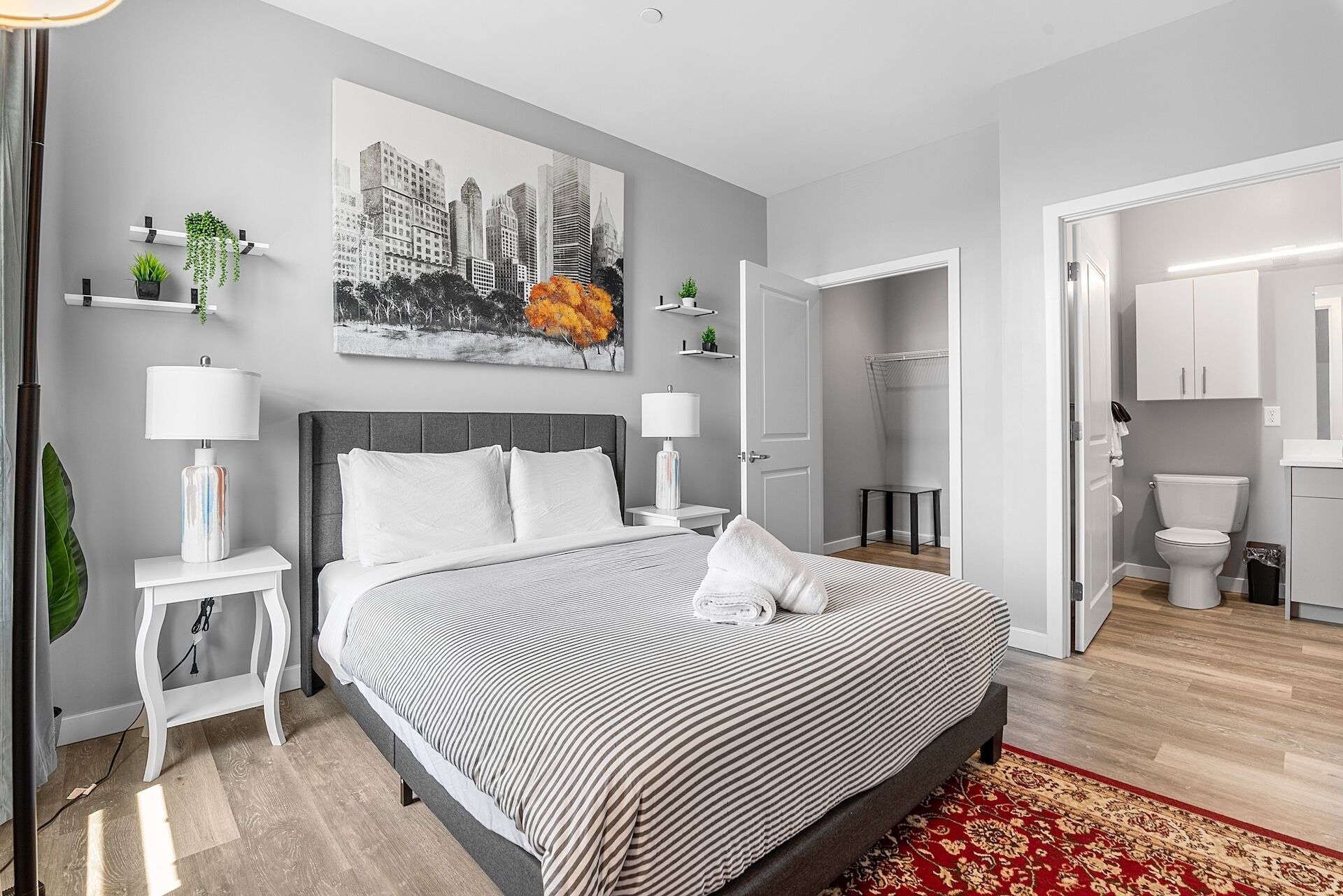 Une chambre à coucher moderne avec un grand lit, des tables de chevet, un tableau représentant un paysage urbain et une vue sur la salle de bain.