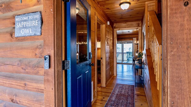 Pasillo interior de madera con una puerta azul, un letrero de bienvenida y vistas a una terraza exterior.