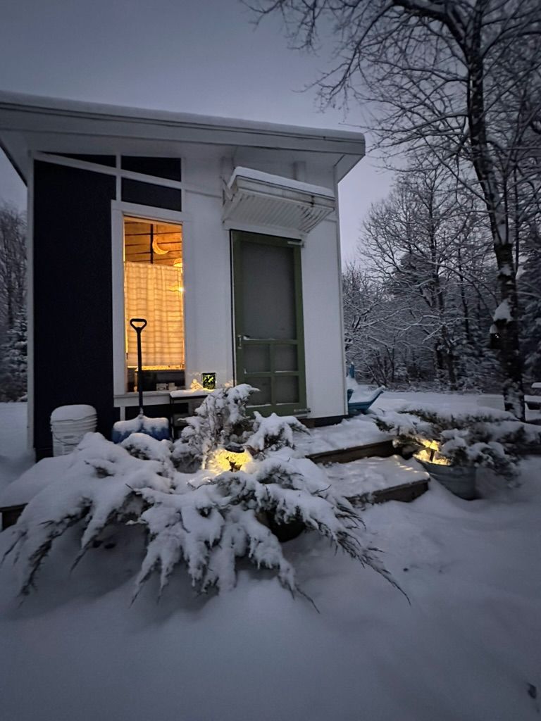 Ein schneebedecktes Haus mit beleuchtetem Eingang und einer kleinen Außenbeleuchtung.