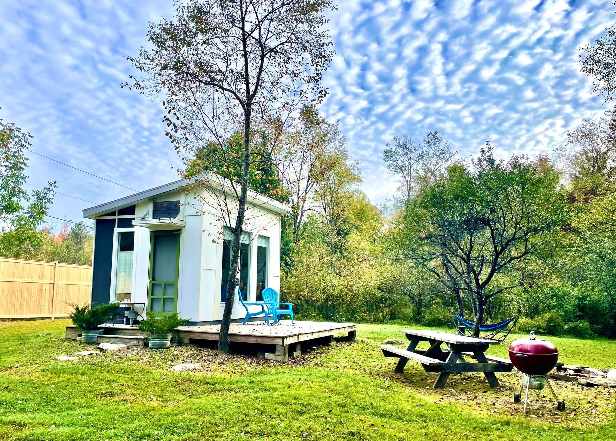 A small house with a deck, a picnic table, and a barbecue grill in a backyard.
