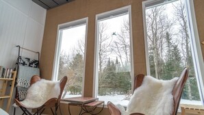 A cozy room with large windows, a wooden table, and two leather chairs with fur throws. - Glamping hut with WiFi in Ripton, biking, hiking, skiing (Ripton)