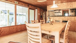 A wooden interior with a dining table, chairs, a hanging light fixture, and a kitchen area. - 6 Person Holiday Home in Dannemare (Dannemare)