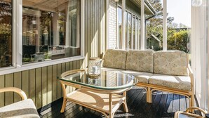 A covered patio with a glass table, wicker furniture, and a view of the house. - 6 Person Holiday Home in Dannemare (Dannemare)