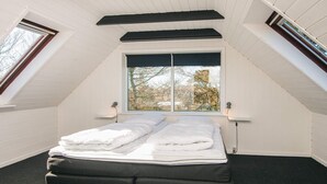 A bedroom with a sloped ceiling, a large window, a bed with white linens, and a black bench. - 5 Person Holiday Home in Snedsted (Snedsted)