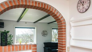 A room with a brick archway, a black sofa, a clock, and a window with a view of trees. - 5 Person Holiday Home in Snedsted (Snedsted)