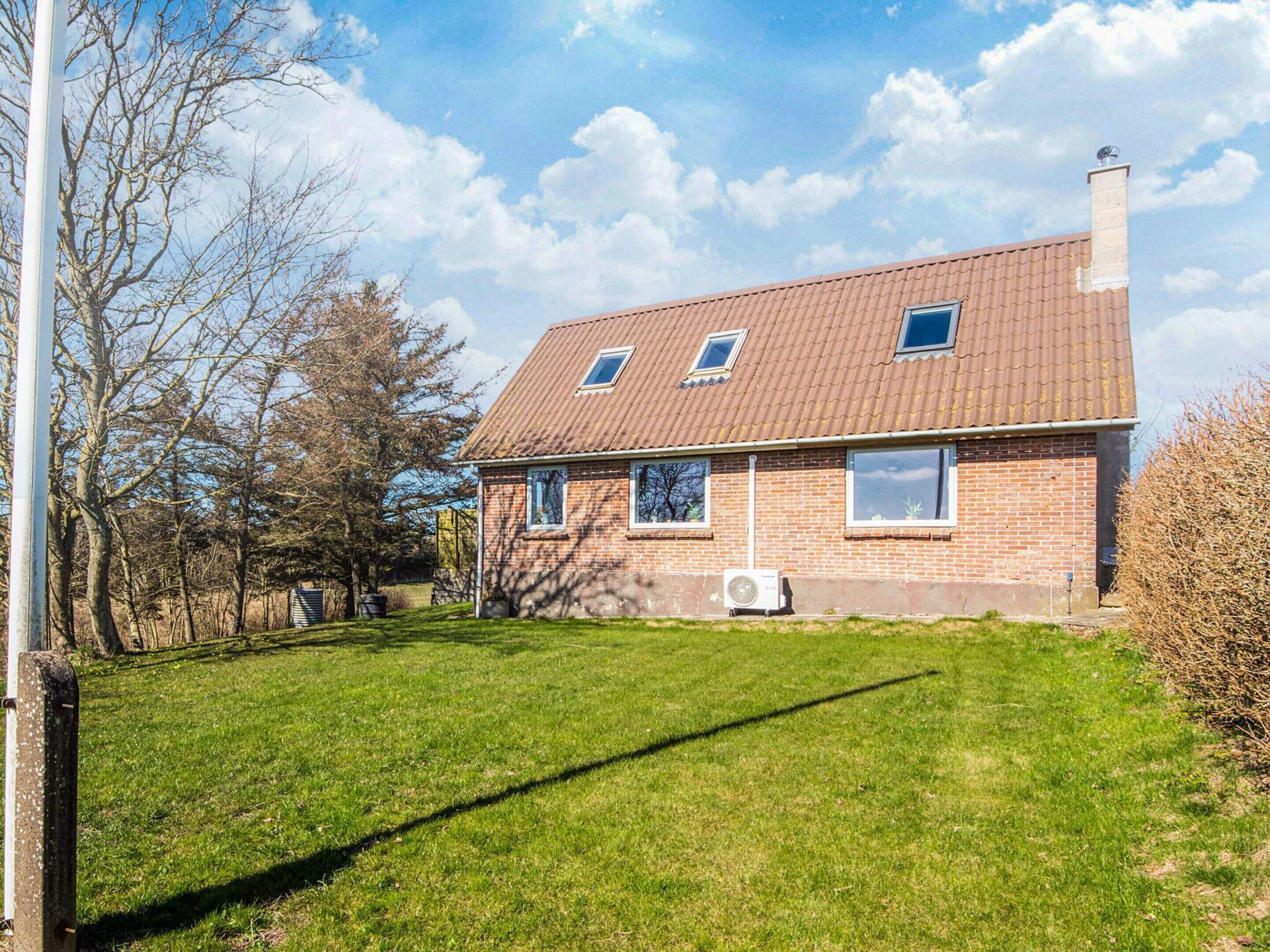 Una casa a due piani in mattoni con tetto spiovente, un camino e un piccolo garage adiacente.
