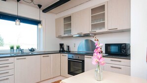 A modern kitchen with light wood cabinets, a stainless steel range hood, a black microwave, and a vase with pink flowers on the counter. - 5 Person Holiday Home in Snedsted (Snedsted)