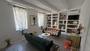 Een woonkamer met een groene bank, een salontafel, vloertegels met een patroon, een boekenkast en een televisie.