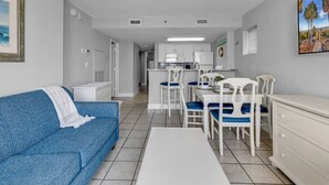 Un espacio habitable compacto con kitchenette, un comedor con sillas blancas y azules, y un sofá azul.