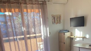 Una habitación con sofá, escritorio, televisor y ventana con cortinas.