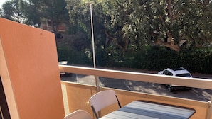 Un balcón con una mesa y sillas, suelo de baldosas y vistas a la calle y árboles.